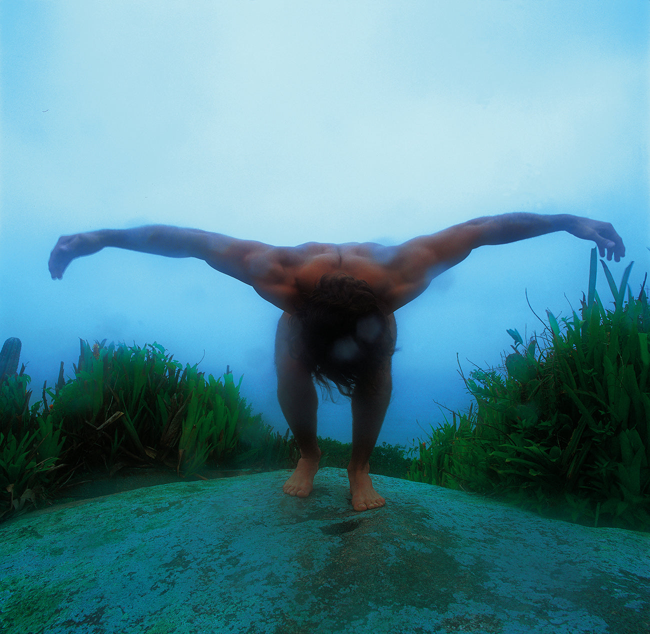 Man in the Rain

On the highest point of a small island in southern Brazil, under a light tropical rain, a strong yet gentle man leans forward, lowering his head and opening his arms like wings. In this suspended moment, he seems to absorb the full energy of the place: the rain, the solid stone beneath his feet, the intense green vegetation, and the distant sea veiled by mist.

Part of the Elemental series, Man in the Rain expresses a deep communion between the human figure and the natural world. His gestur